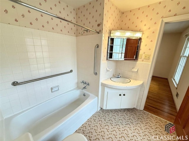 full bath with tile walls, a wainscoted wall, wallpapered walls, vanity, and shower / washtub combination