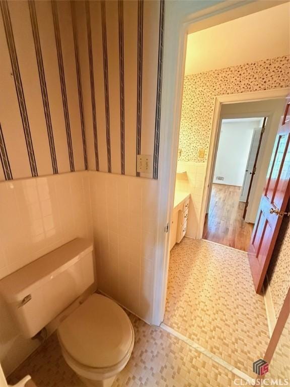 bathroom featuring tile walls, wallpapered walls, and toilet