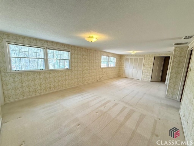 empty room featuring visible vents, a textured ceiling, wallpapered walls, and light carpet