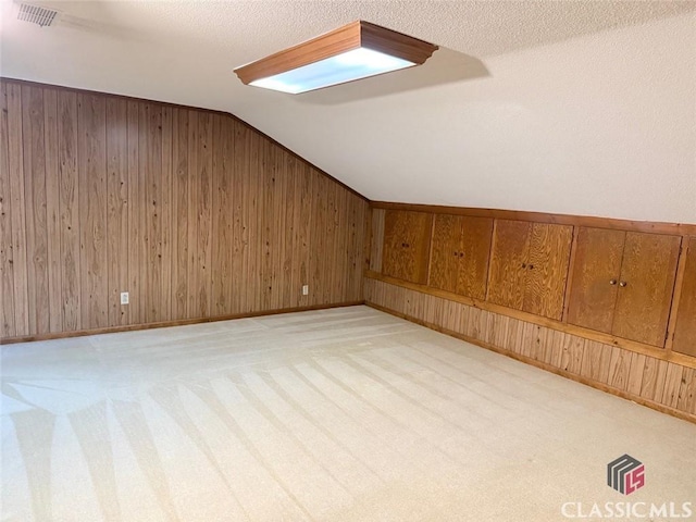 additional living space featuring visible vents, light carpet, lofted ceiling, and wooden walls