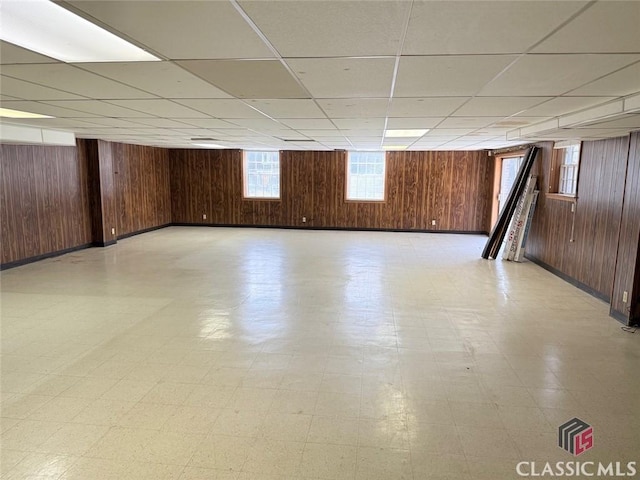 below grade area with a paneled ceiling, wooden walls, and light floors