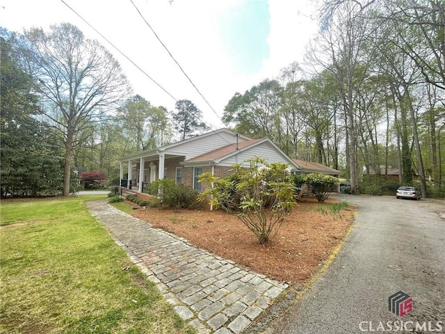 view of side of property with driveway, covered porch, and a yard