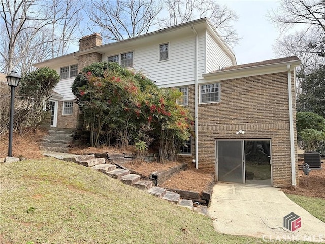 rear view of house featuring brick siding, a yard, a chimney, and central air condition unit