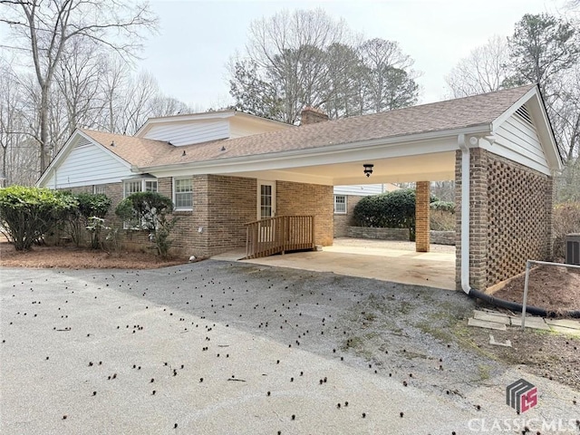 exterior space with driveway, a chimney, an attached carport, and brick siding