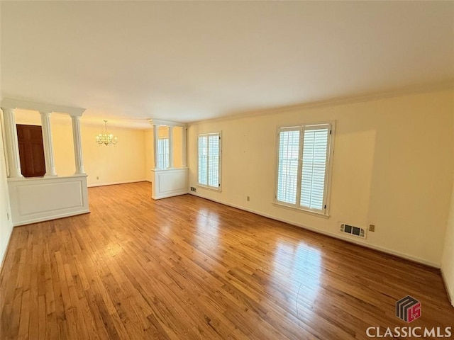 spare room featuring ornate columns, visible vents, an inviting chandelier, light wood-style floors, and baseboards