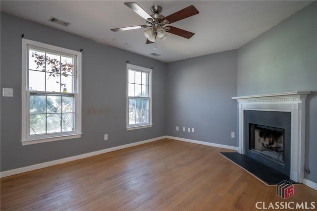 unfurnished living room with a fireplace with raised hearth, light wood-type flooring, visible vents, and baseboards