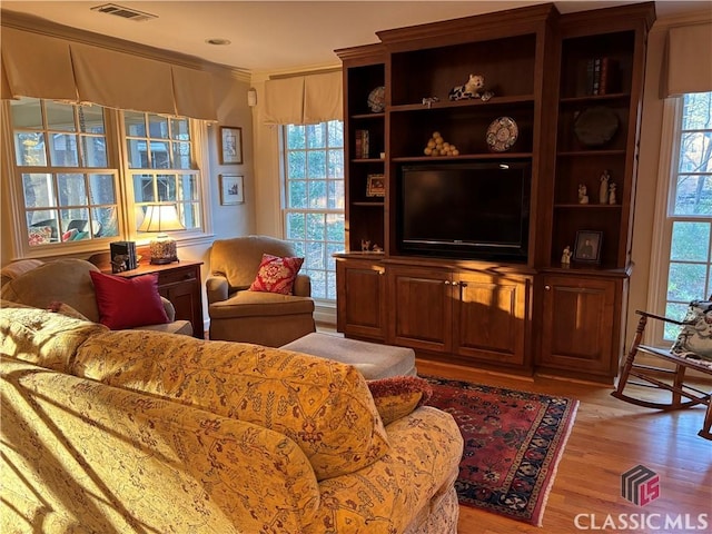 living area featuring a wealth of natural light, light wood-style flooring, visible vents, and crown molding