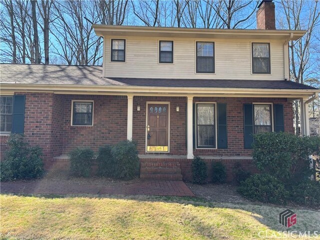 view of front of property featuring brick siding, a chimney, a porch, and a front lawn