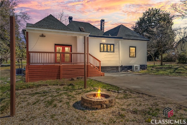 rear view of house featuring a fire pit, concrete driveway, french doors, and roof with shingles