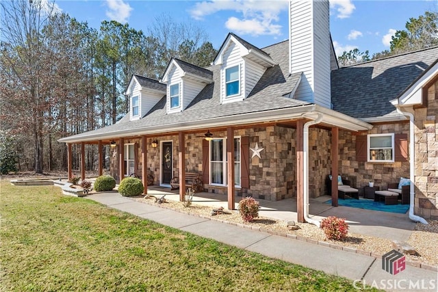 view of front facade with covered porch, a shingled roof, stone siding, a front lawn, and a chimney