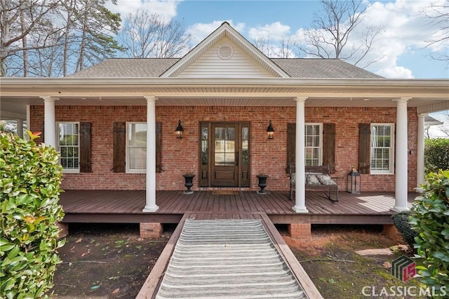 exterior space with a shingled roof, a porch, and brick siding