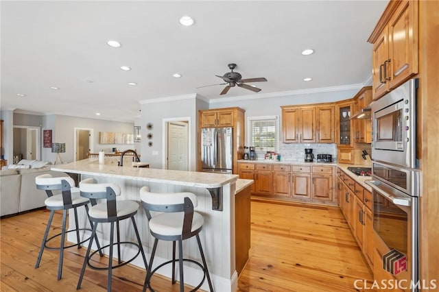 kitchen with brown cabinets, appliances with stainless steel finishes, open floor plan, a kitchen island with sink, and a kitchen bar