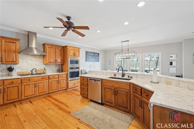 kitchen featuring stainless steel appliances, a sink, brown cabinets, wall chimney exhaust hood, and pendant lighting