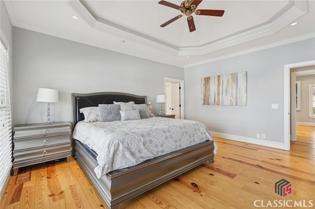 bedroom featuring ornamental molding, a tray ceiling, baseboards, and wood finished floors