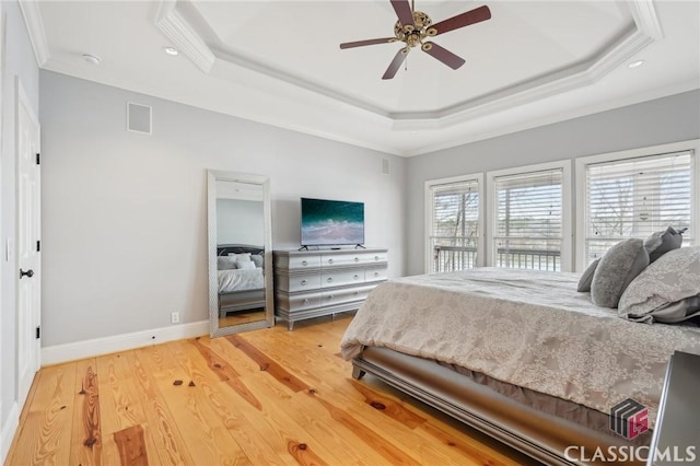 bedroom with crown molding, a raised ceiling, visible vents, wood finished floors, and baseboards