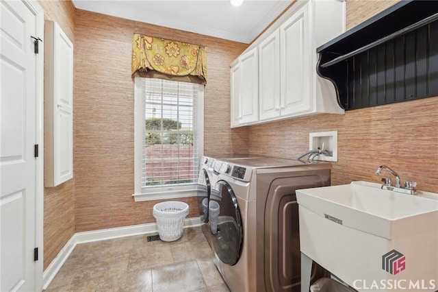 washroom featuring crown molding, washing machine and clothes dryer, cabinet space, a sink, and baseboards