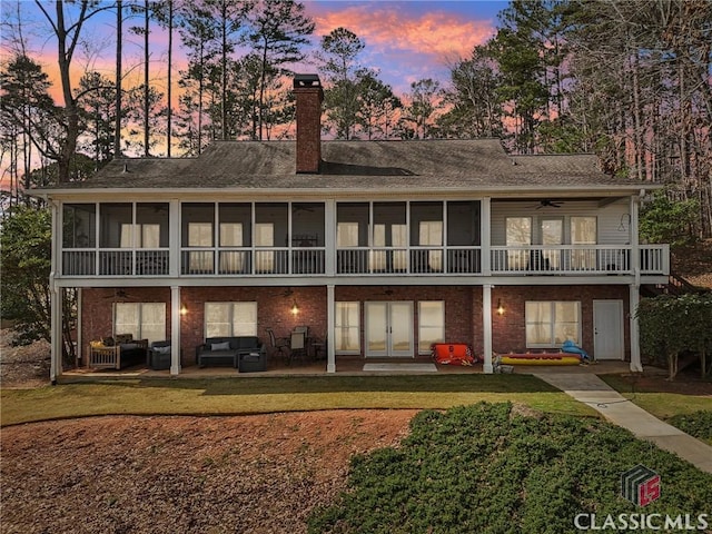 back of property at dusk with an outdoor hangout area, a patio, a yard, and a chimney