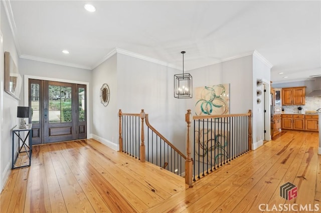 foyer with ornamental molding, light wood-type flooring, a chandelier, and baseboards