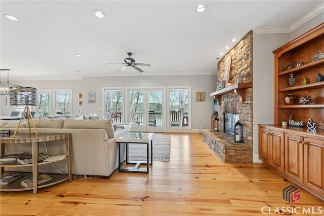 living area featuring light wood-type flooring, crown molding, a stone fireplace, and recessed lighting