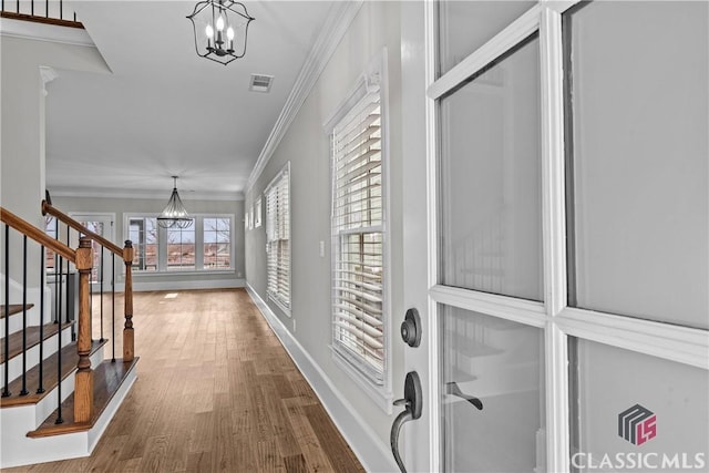 hallway with a notable chandelier, wood finished floors, baseboards, ornamental molding, and stairway