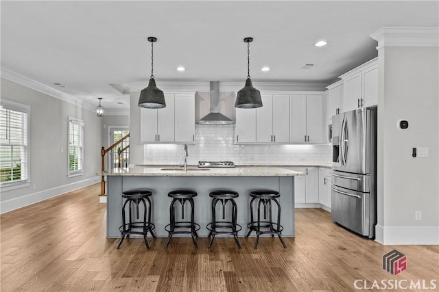 kitchen featuring stainless steel fridge with ice dispenser, a kitchen island with sink, crown molding, wall chimney range hood, and a sink