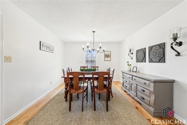 dining area featuring a textured ceiling, light wood finished floors, baseboards, and an inviting chandelier