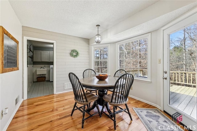 dining area with baseboards, visible vents, light wood-style flooring, a textured ceiling, and wood walls