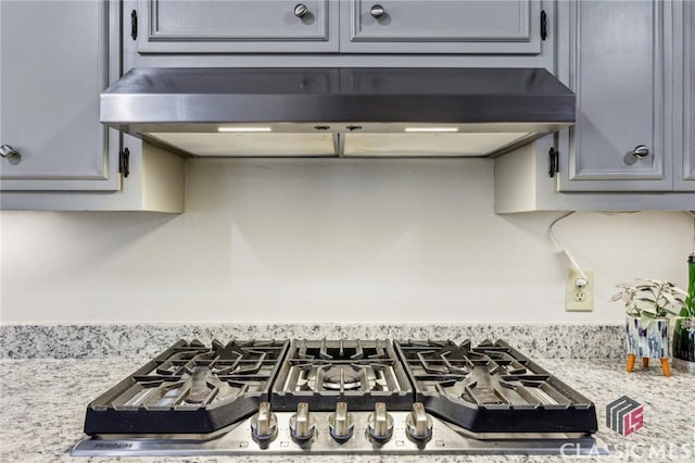 kitchen with light stone countertops, stainless steel gas cooktop, extractor fan, and gray cabinetry