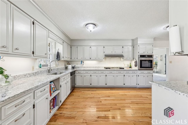 kitchen featuring under cabinet range hood, a sink, appliances with stainless steel finishes, light stone countertops, and light wood finished floors