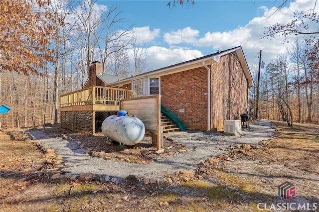 view of side of home featuring brick siding, a chimney, and a wooden deck