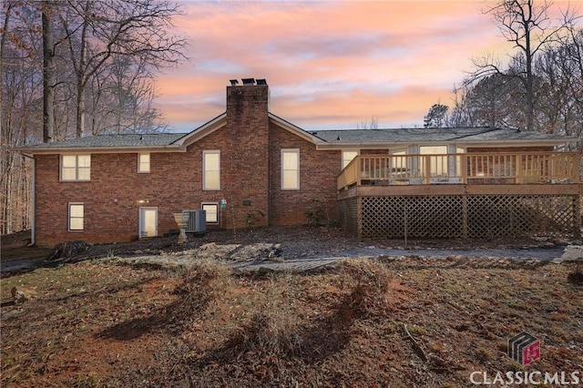 rear view of house with a chimney, a deck, cooling unit, and brick siding