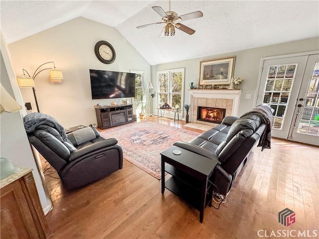 living area featuring a tile fireplace, ceiling fan, vaulted ceiling, a textured ceiling, and light wood-style floors