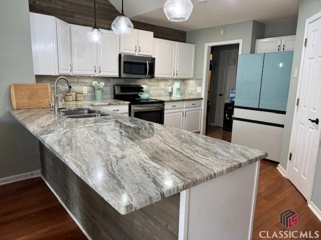 kitchen with light stone counters, stainless steel appliances, white cabinetry, a sink, and a peninsula