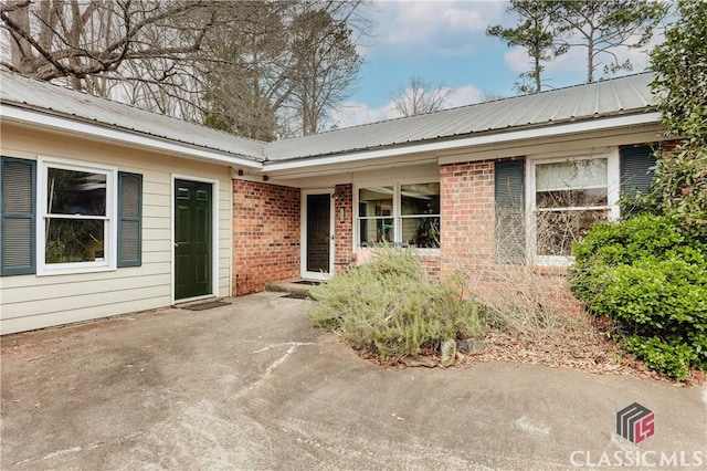 view of exterior entry featuring metal roof, brick siding, and a patio