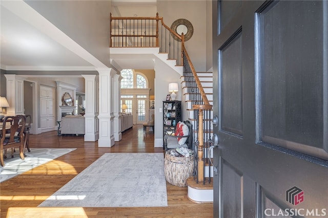 entryway with stairway, wood finished floors, a towering ceiling, and ornate columns