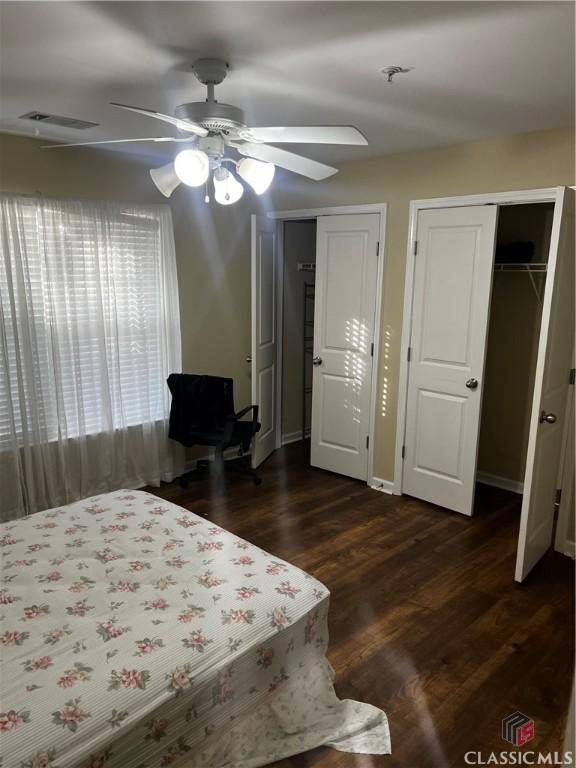 bedroom featuring dark wood finished floors, multiple closets, visible vents, a ceiling fan, and baseboards