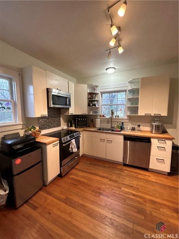 kitchen with appliances with stainless steel finishes, light countertops, white cabinetry, open shelves, and a sink