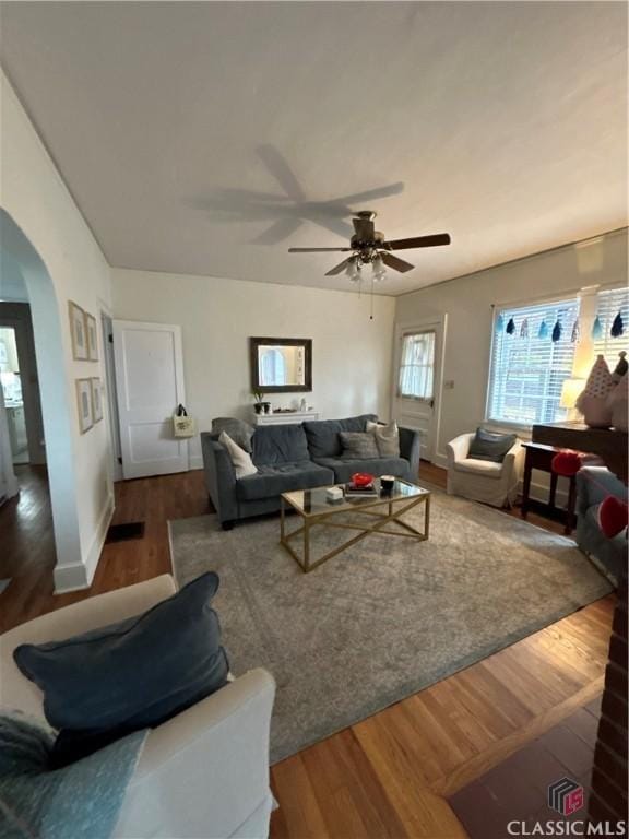 living area featuring arched walkways, wood finished floors, and a ceiling fan