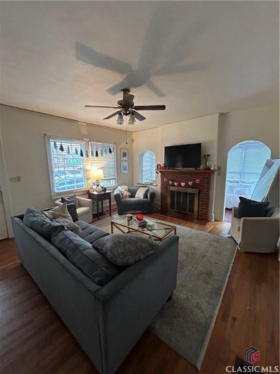 living area with dark wood-style floors, ceiling fan, and a brick fireplace