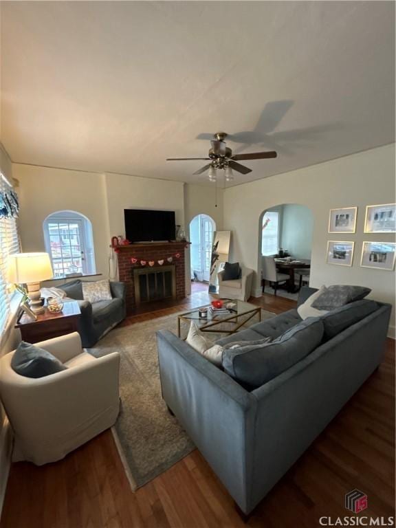 living room with arched walkways, a fireplace, plenty of natural light, and wood finished floors