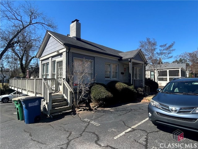 view of home's exterior with uncovered parking, brick siding, and a chimney