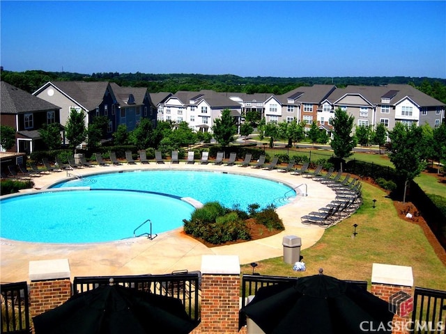 community pool with a lawn, a patio area, and a residential view