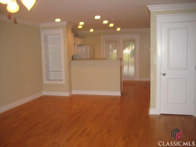 unfurnished living room with a chandelier, ornamental molding, wood finished floors, and baseboards