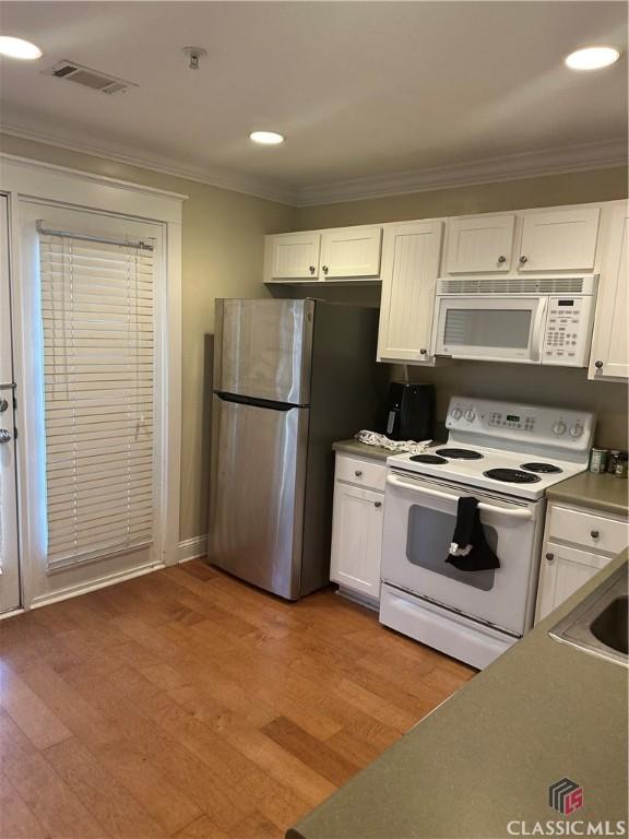 kitchen featuring crown molding, white cabinets, a sink, wood finished floors, and white appliances