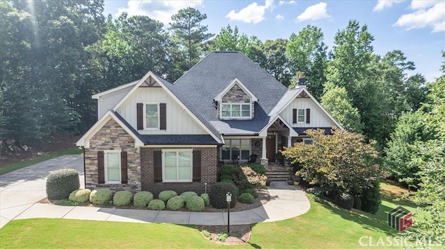 craftsman-style house with brick siding, a shingled roof, board and batten siding, a front yard, and stone siding