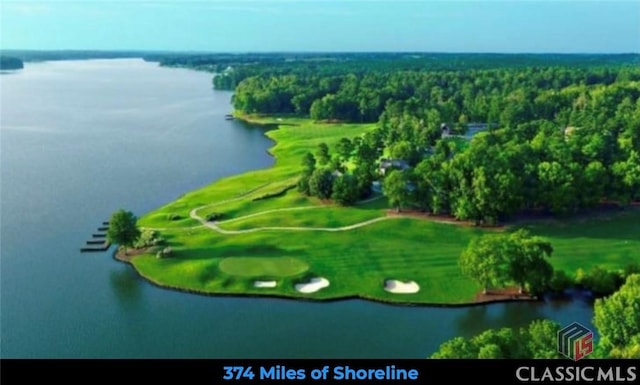 drone / aerial view with view of golf course, a water view, and a view of trees