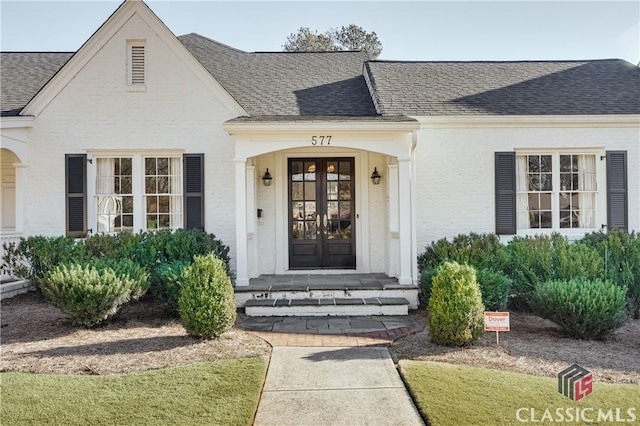 doorway to property with french doors, roof with shingles, and brick siding