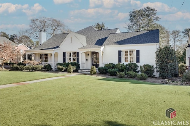 view of front of property featuring roof with shingles, a front lawn, and a chimney