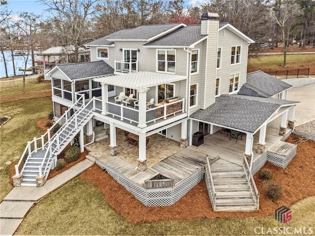 rear view of house with a sunroom, a chimney, stairway, roof with shingles, and a deck