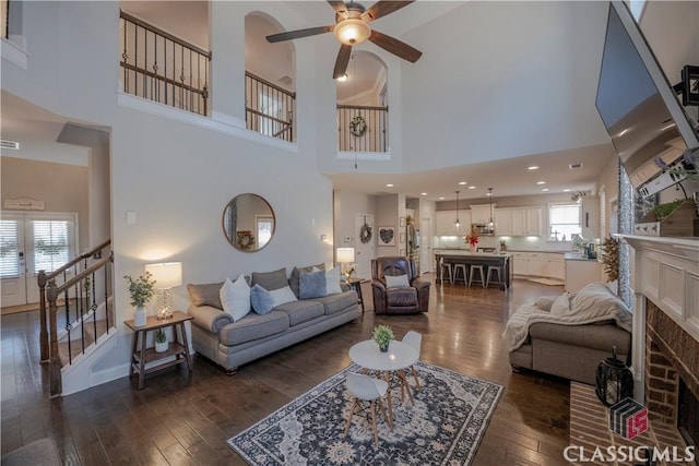 living area featuring a brick fireplace, a wealth of natural light, stairs, and dark wood-type flooring